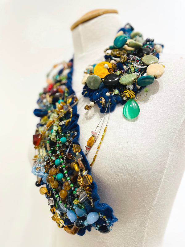 This colourful felted neckpiece incorporates vintage plastic costume jewellery and doilies to make a bold and playful statement. The blue felted underside is soft against the skin, with a comfortable weight.