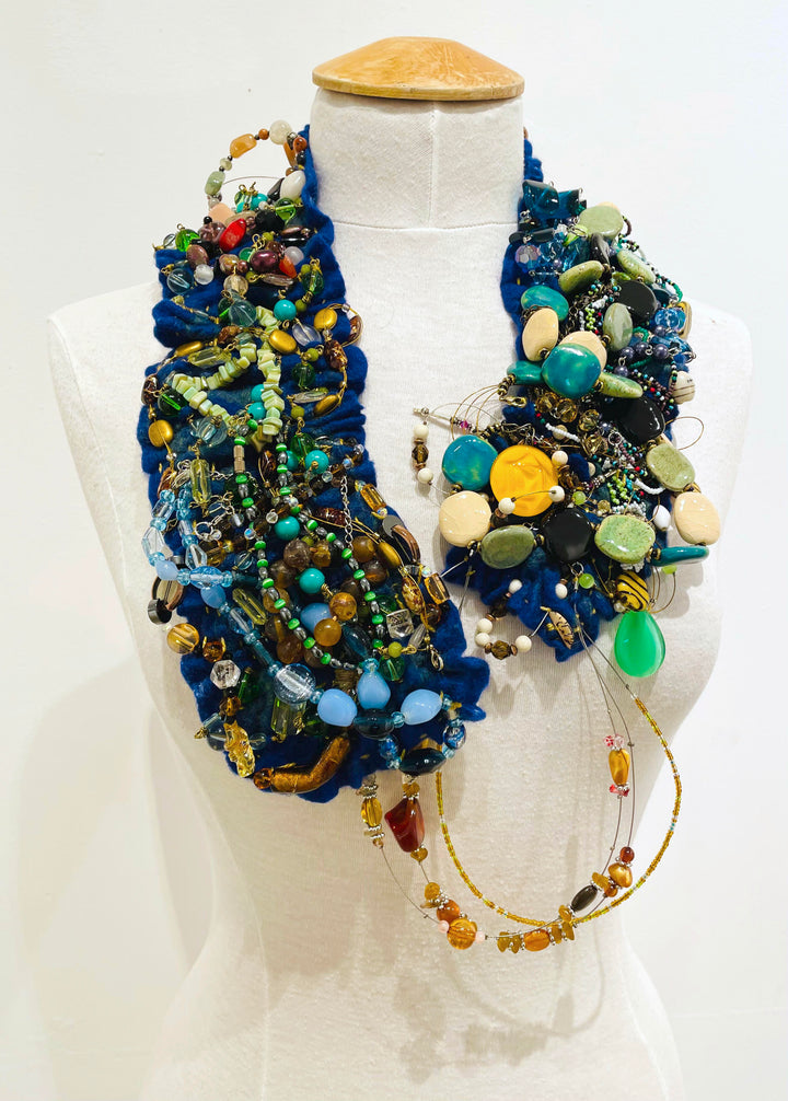 This colourful felted neckpiece incorporates vintage plastic costume jewellery and doilies to make a bold and playful statement. The blue felted underside is soft against the skin, with a comfortable weight.