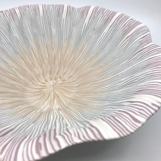Multicolour ceramic bowl with strands of yellow, blue, and pink extending from the center to the rippled edges, made with the nerikomi ceramic technique.