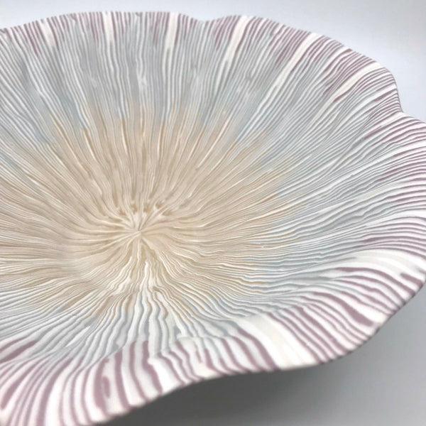 Multicolour ceramic bowl with strands of yellow, blue, and pink extending from the center to the rippled edges, made with the nerikomi ceramic technique.