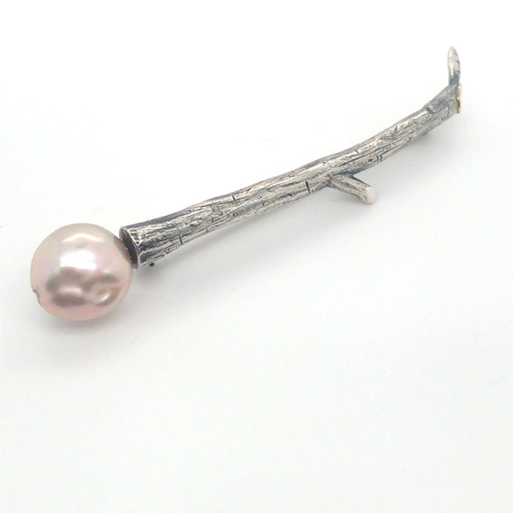 Twig brooch. The sterling silver form is capped at one end by a natural pink pearl, and at the other by a small gold detail where a tiny leaf branches off. 6.5 x 1.2 x 0.7 cm.