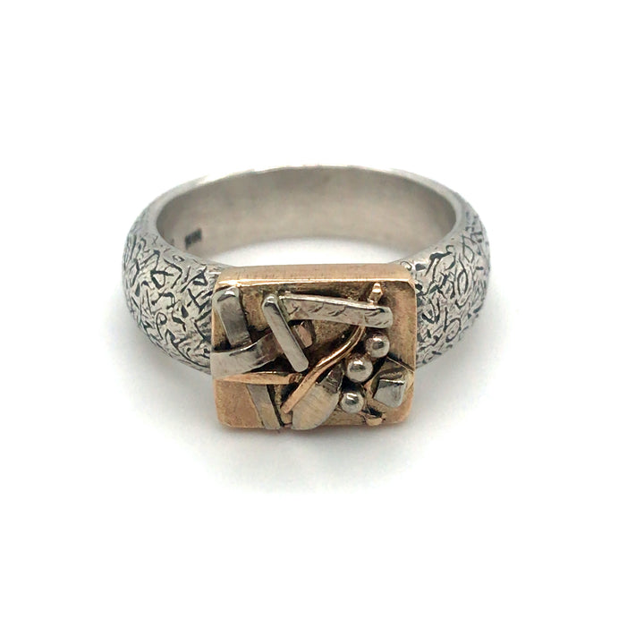 One of a kind ring in 10k yellow gold with a textured sterling silver band. Small details on the face in silver and gold suggest leaves and twigs. 2.3 x 2.1 x 0.8 cm.
