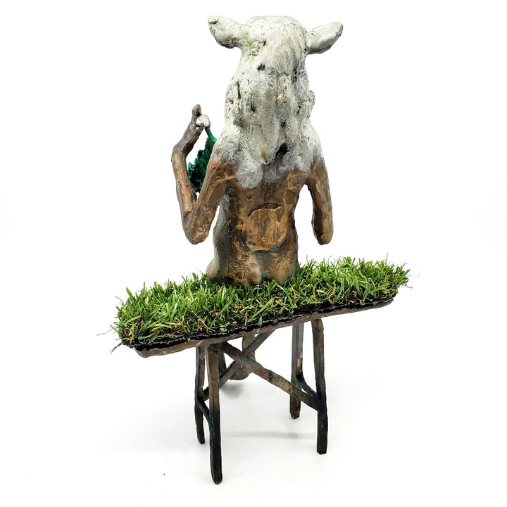 Domestic Sheep: Elsie Mae.  A bronze figure with a sheep's head and a woman's body sits on a turf-covered bench, peacefully knitting. 1 of 1.