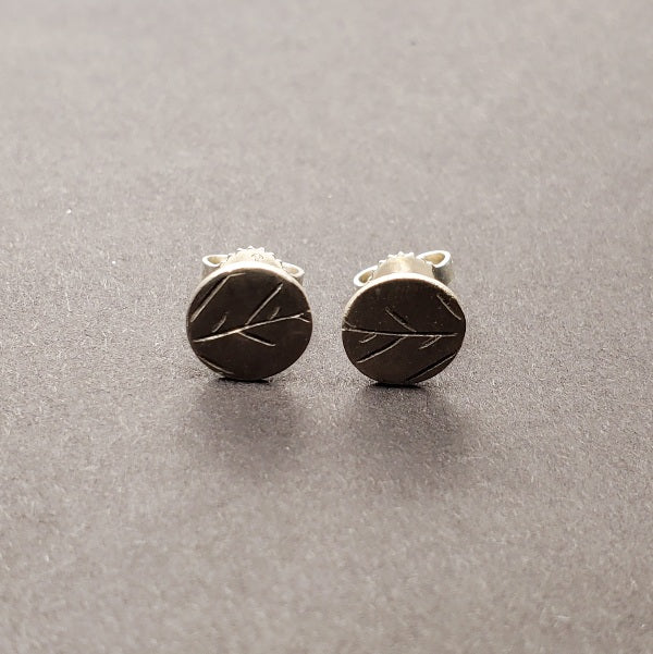 Tiny circular stud earrings in sterling silver with the delicate tracing of twigs on the surface.