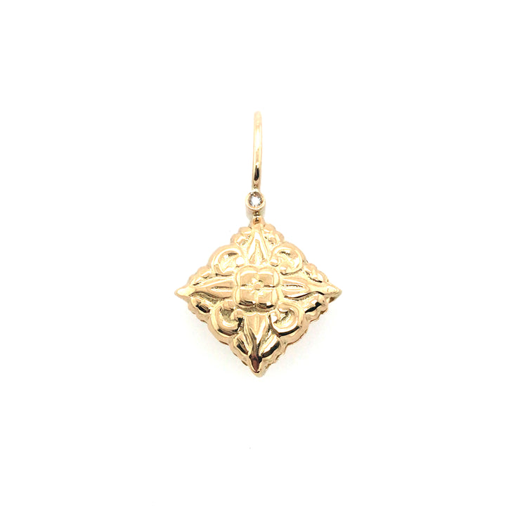 Double-sided pendant that is slightly pillowed in 18k gold with a diamond on each side of the Nepalese flower stamp