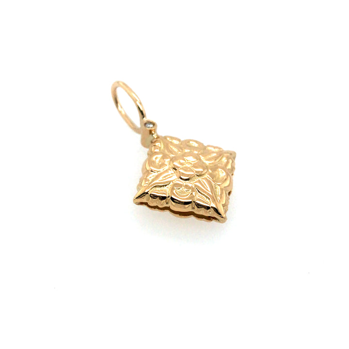 Double-sided pendant that is slightly pillowed in 18k gold with a diamond on each side of the Nepalese flower stamp