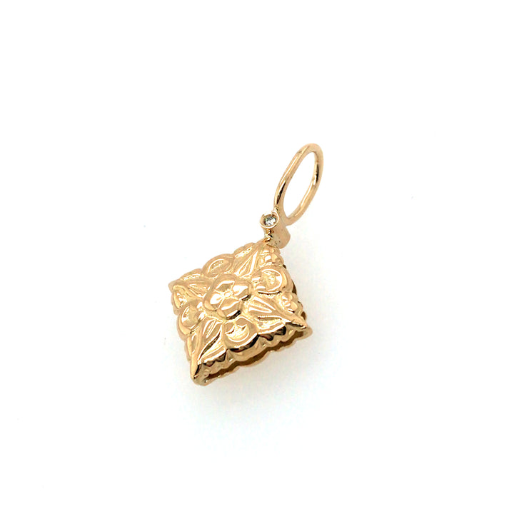 Double-sided pendant that is slightly pillowed in 18k gold with a diamond on each side of the Nepalese flower stamp