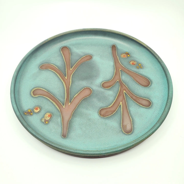 Large circular ceramic platter with a green decorated surface revealing the red clay.