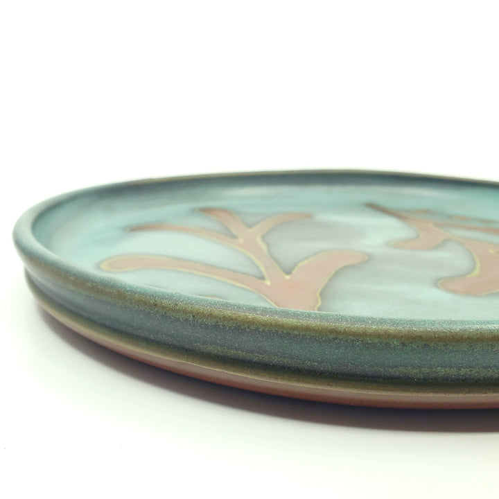 Large circular ceramic platter with a green decorated surface revealing the red clay.