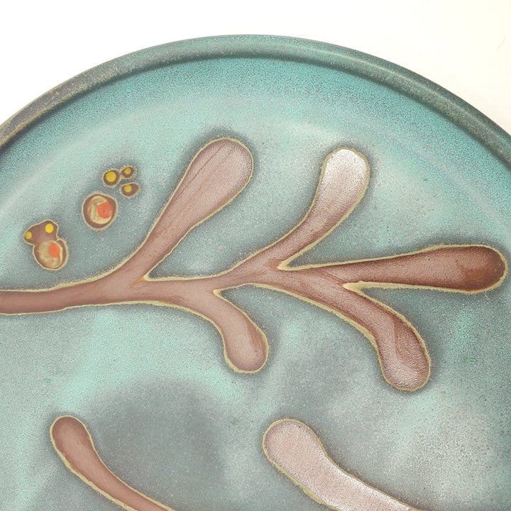 Large circular ceramic platter with a green decorated surface revealing the red clay.