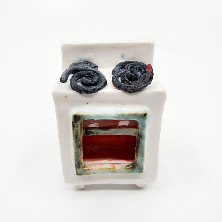 Cake Wife: Two-part ceramic sculpture of a woman holding a cake, and an oven. Designed to hang on the wall, each hangs separately from a metal loop.