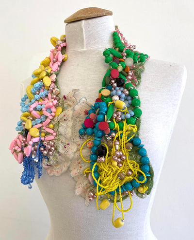 This colourful felted neckpiece incorporates vintage plastic costume jewellery and doilies to make a bold and playful statement. The green felted underside is soft against the skin, with a comfortable weight.