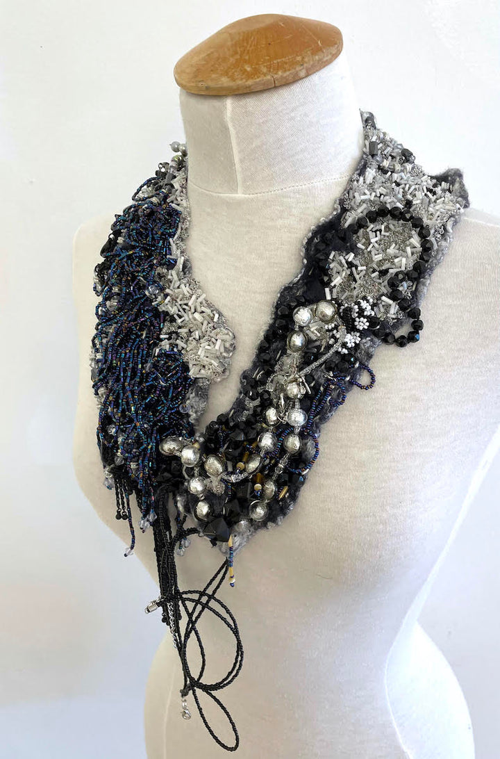 This shimmering felted neckpiece incorporates swatches of beaded fabrics and jewellery to make a bold, stylish statement. The blue-grey felted underside is soft against the skin, with a comfortable weight.