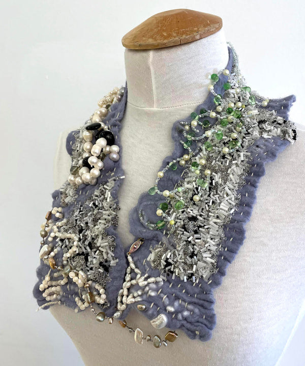 This shimmering felted neckpiece incorporates swatches of beaded fabrics and jewellery as well as lengths of pearls to make an elegant statement. The blue-grey felt is soft against the skin, with a comfortable weight.
