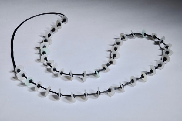 Necklace of stacked flat glass beads in soft grey with black rubber cord, 40". The 40 beads are around 1.5cm in diameter.