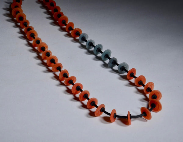 Necklace of stacked flat glass beads in red and grey with black rubber cord, 30". The 40 beads are around 1.5cm in diameter.