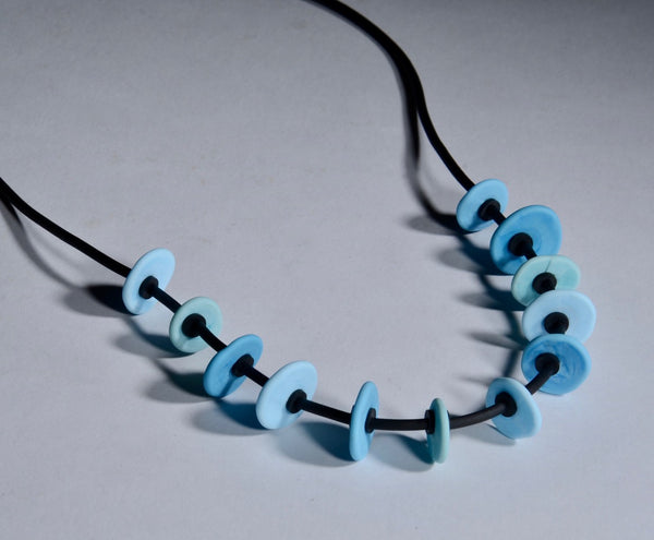 Necklace of stacked flat glass beads in aqua/turquoise blue with black rubber cord, 24". The 12 beads are around 1.5cm in diameter.