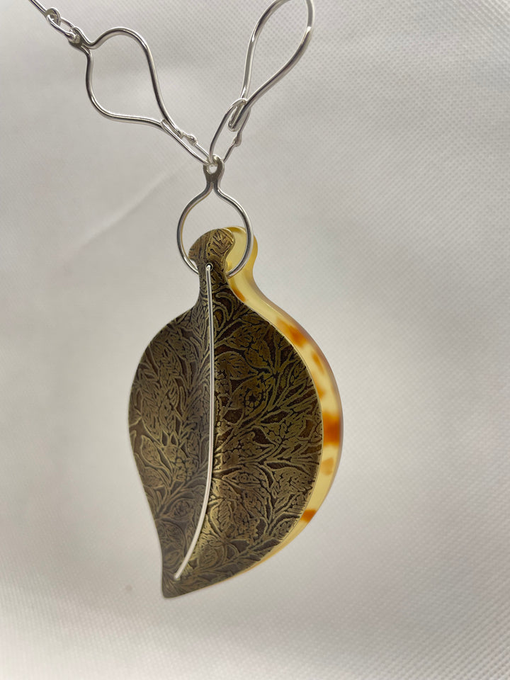 Leaf pendant of etched brass and light brown cellulose acetate. The brass and acetate leaves are "sewn" together with silver wire. The pendant hangs from a chain sterling silver chain with leaf-shaped links.