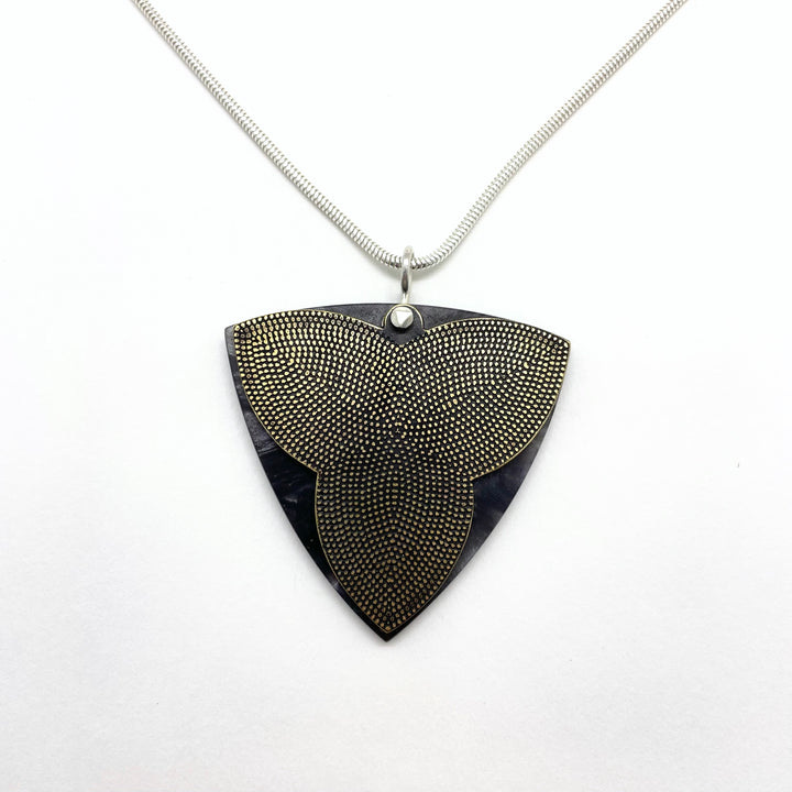 Rounded triangle pendant of etched brass with dotted pattern and black & grey cellulose acetate. A sterling rivet holds the two pieces together.