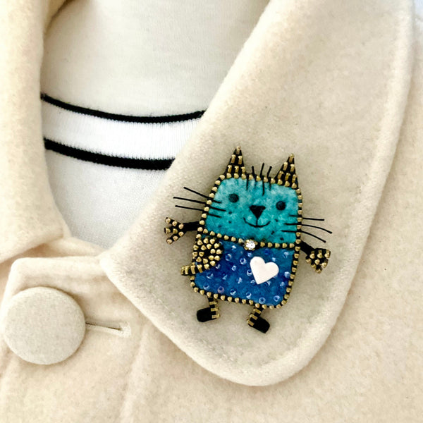 Blue cat brooch with a heart on a beige coat