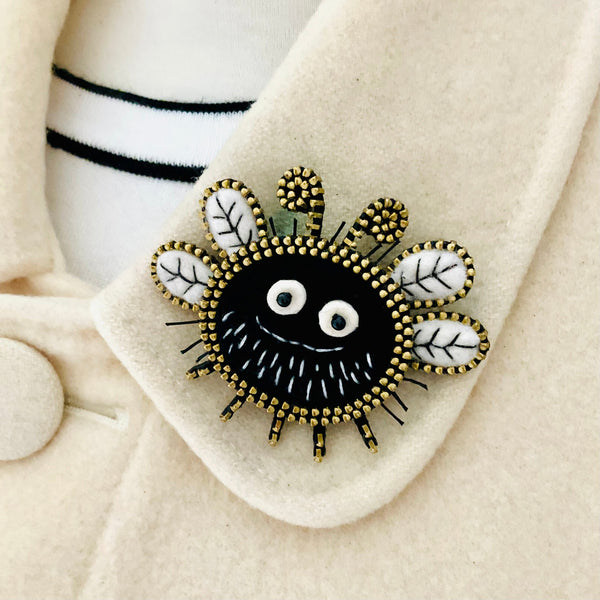 Black and gold brooch with white accents on a beige coat