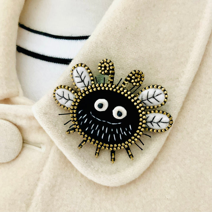 Black and gold brooch with white accents on a beige coat