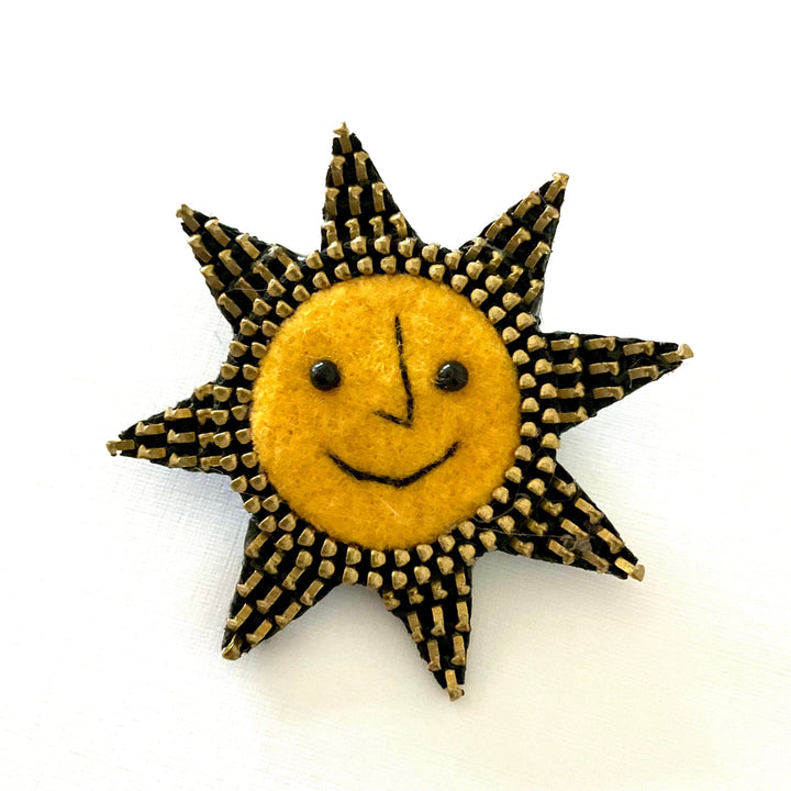 Sun-shaped brooch with a smiling face on a white background