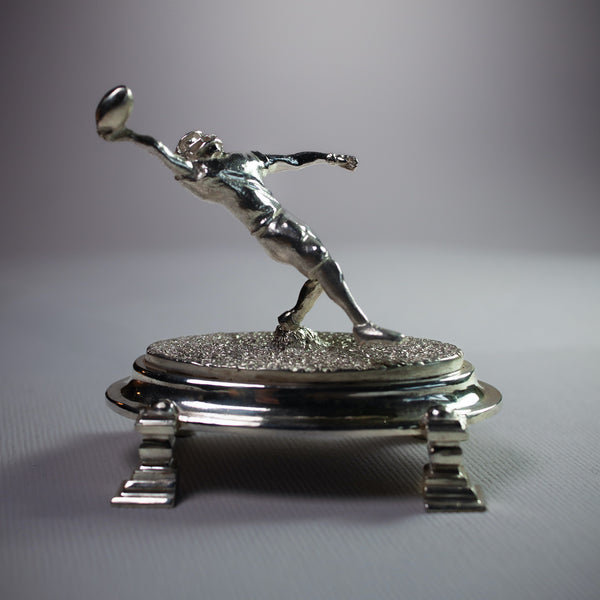 Silver sculpture of a figure in action on a stand 