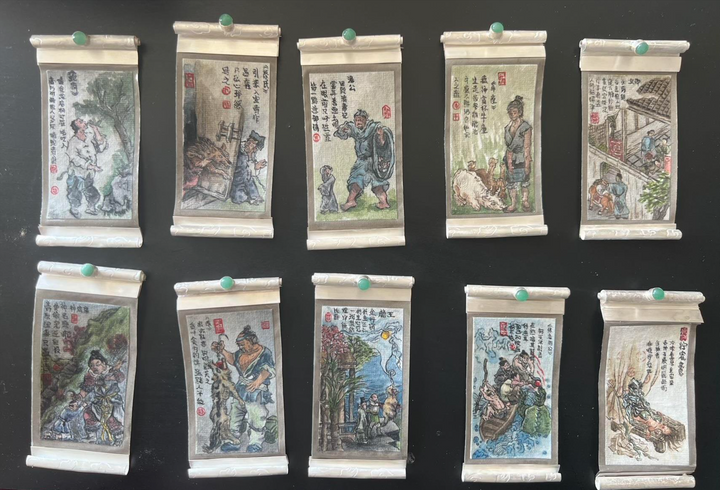 Set of small scroll painting brooches with various scenes and characters on a black background