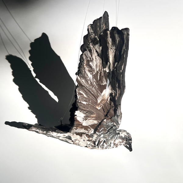 Parasitic Jaeger in Flight - wings up : multi-fired porcelain suspended sculpture of a jaeger in flight, its wings reaching upwards. The surface is richly decorated with texture.