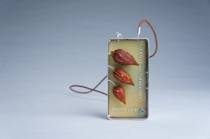 Mom's love #6 necklace, 2023.  Created with fabrication, cloisonné enamel on copper, and basel setting, this necklace is made of copper, silver, lather, topaz, and a found object (gardenia).   3.5x2x0.5 inches