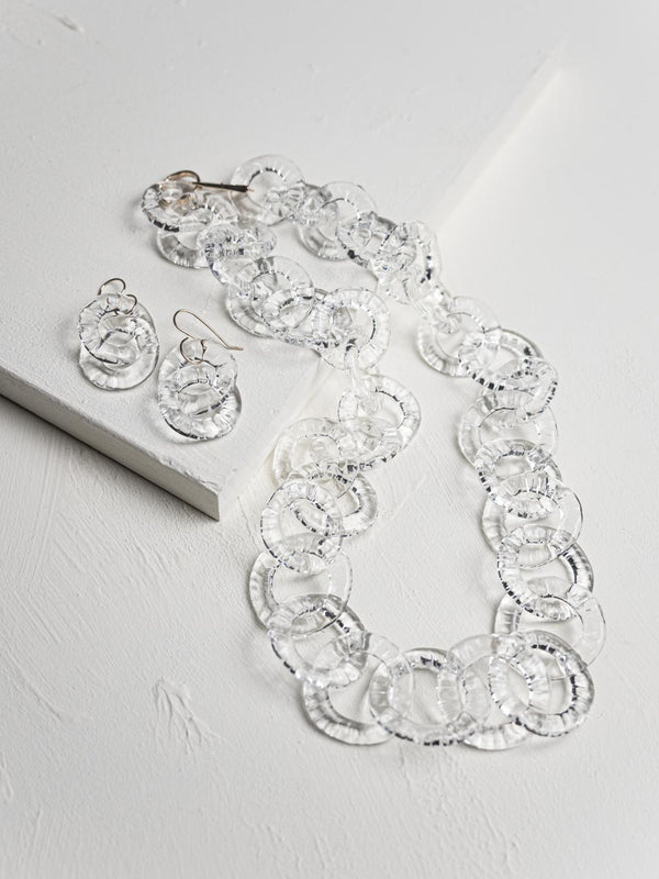 Necklace and earrings set with clear circular stones on a light gray background