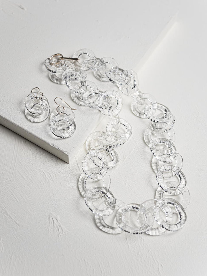 Necklace and earrings set with clear circular stones on a light gray background