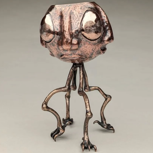 Metallic sculpture of a character with large eyes and thin legs on a gray background