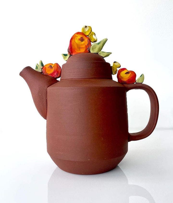 Cheerful red clay ceramic teapot with floral details.