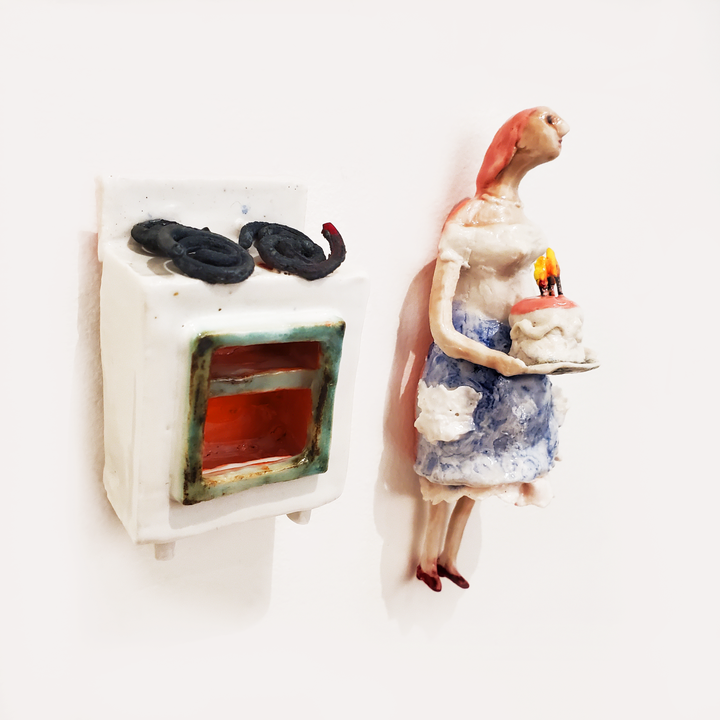 Cake Wife: Two-part ceramic sculpture of a woman holding a cake, and an oven. Designed to hang on the wall, each hangs separately from a metal loop.