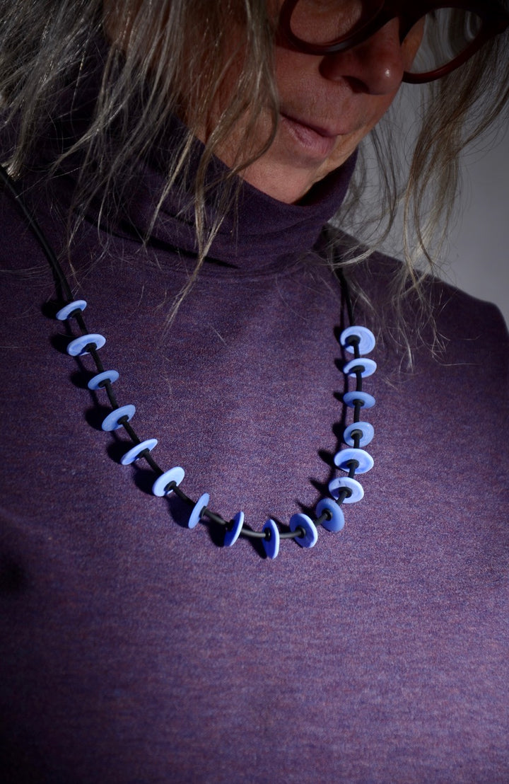 Necklace of stacked flat glass beads in periwinkle blue with black rubber cord, 30". The 17 beads are around 1.5cm in diameter.