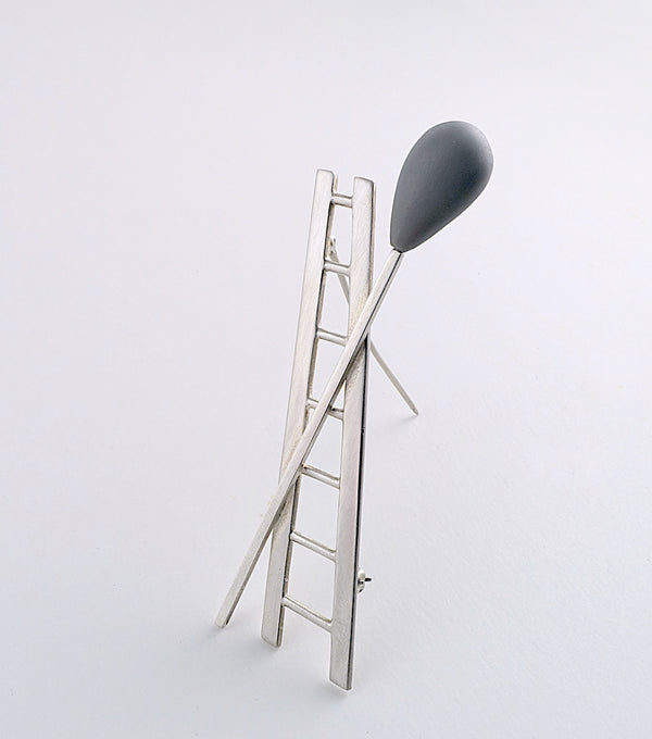 The clean lines of a leaning silver ladder of this brooch are perfectly countercrossed by a mysterious balloon of grey resin.