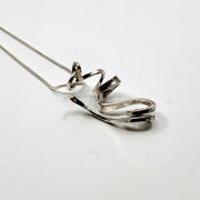 A ribbon-like hand forged sterling silver pendant on a 22" snake chain with a magnetic clasp. 6 x 3 x 1.5 cm