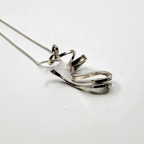 A ribbon-like hand forged sterling silver pendant on a 22" snake chain with a magnetic clasp. 6 x 3 x 1.5 cm