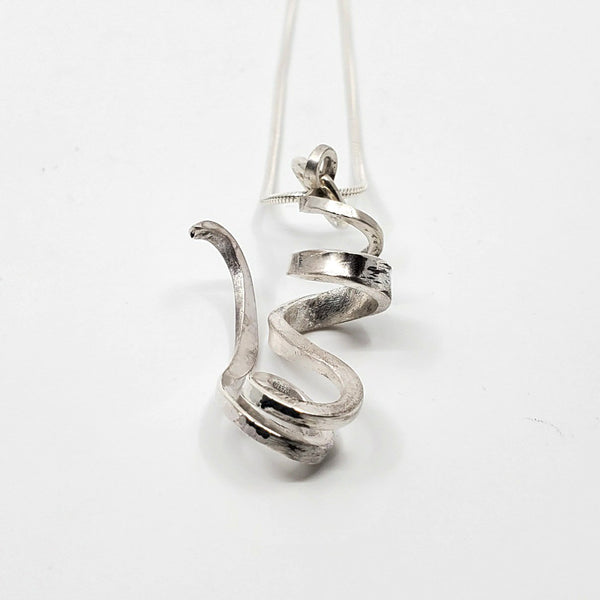 A ribbon-like hand forged sterling silver pendant on a 22" snake chain with a magnetic clasp. 6 x 3 x 1.5 cm