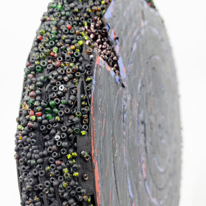 Blue & Black: Mixed media wall sculpture constructed with a corrugated cardboard base. It is painted with acrylics, and adorned with green and red glass beads.