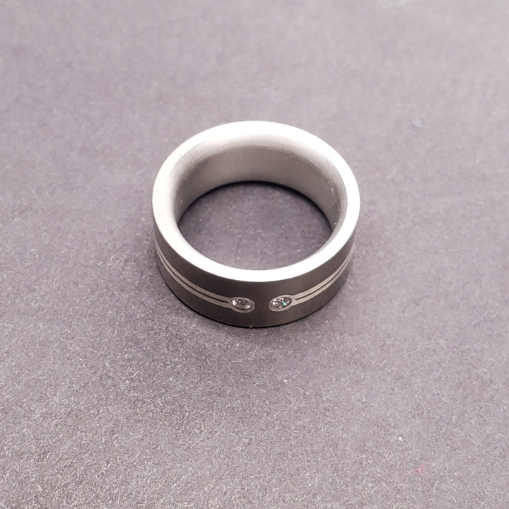 Two 0.025ct reclaimed diamonds are set into one side of this 8mm titanium band, creating a pause in the inlaid fine silver line which circles the form. Size 5 3/4. 