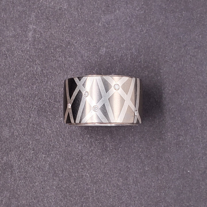 Five 0.01ct reclaimed diamonds are set into the inlaid fine silver lines that criss-cross this 10.5mm titanium band. Size 5.