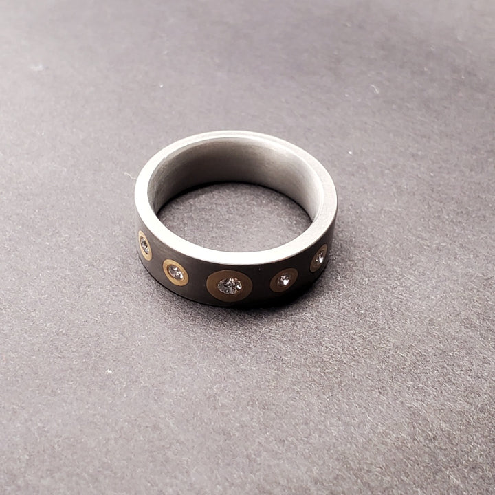 Five circles of inlaid 14k yellow gold dotted with 0.17ct reclaimed diamonds (5 total) seem to glow within this 6mm titanium band. Size 6.