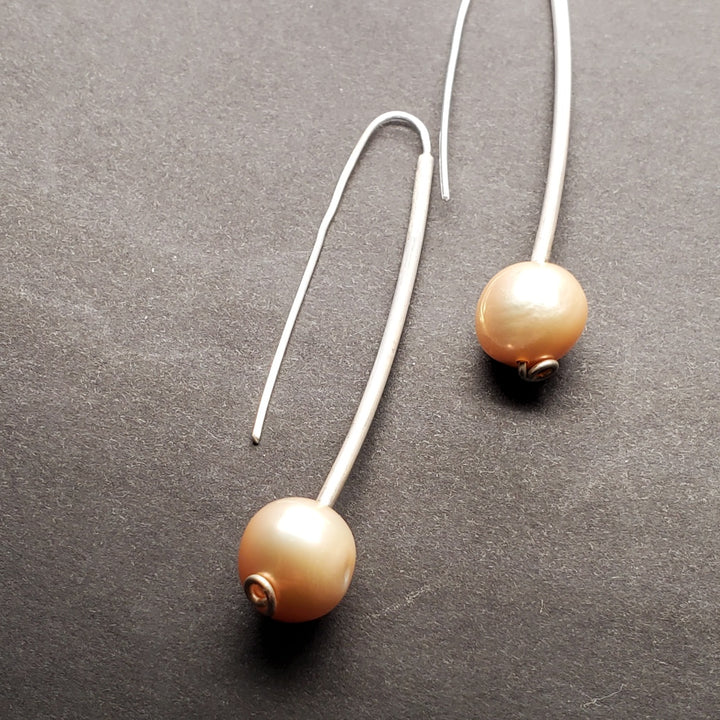 Freshwater pearl dangle earrings with hand formed sterling silver. The 10mm peachy-pink pearls hang gently from long hooks.