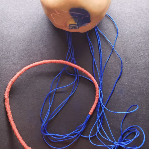 Pendant of porcelain, aluminum, and gold leaf, with nylon cord.