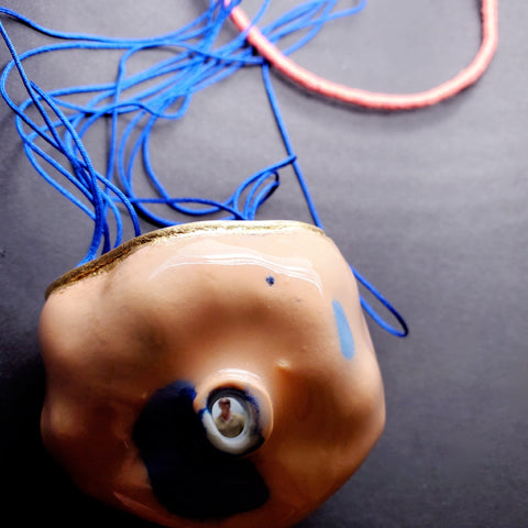 Pendant of porcelain, aluminum, and gold leaf, with nylon cord.