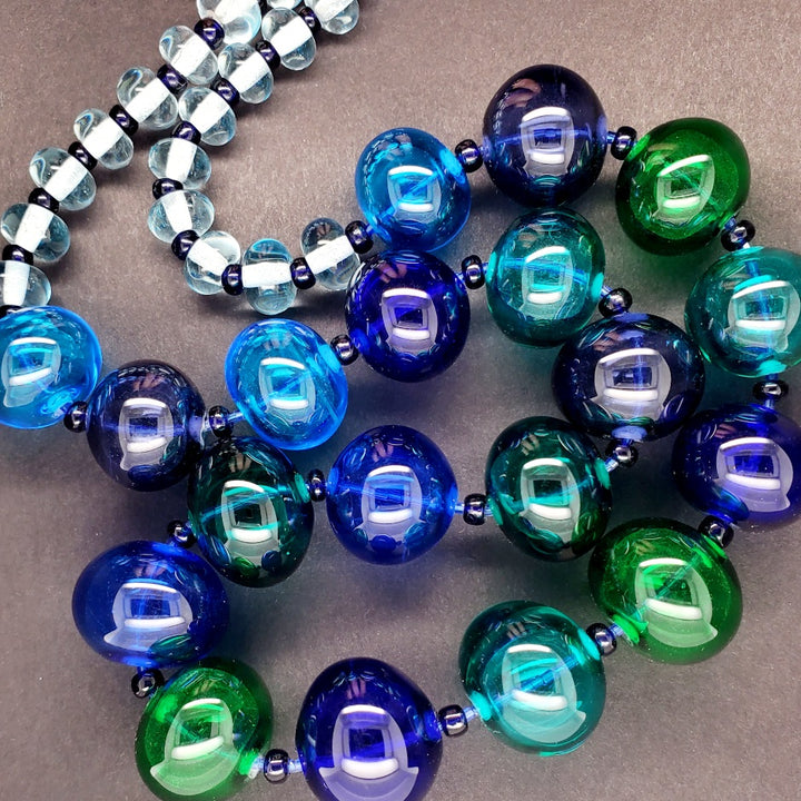 Hollow beaded necklace with sead beeds in various shades of blue made from flameworked glass on a 20" chain with sterling silver clasp.