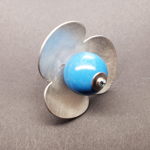 Ring with a large blue bead topped with a blue topaz rests amid 3 large rounded petals of sterling silver, 4 x 2 cm.